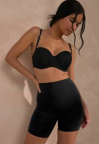 Reggiseno imbottito nero con spalline sottili abbinato a pantaloni corti neri a vita alta. Tessuto liscio con un design aderente e bordi senza cuciture.