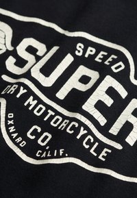 Tela negra con un diseño gráfico blanco agrietado. El texto incluye "SUPER SPEED DRY MOTORCYCLE CO." y "OXNARD CALIF." en letras negritas.