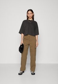 Crni skraćeni majica s širokim rukavima, uparen s cargo hlačama u khaki boji. Model drži pahuljastu crnu clutch torbicu, nosi srebrne platforme čizme.