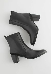 Bottines en cuir noir avec une finition lisse, un bout pointu et un talon bloc. Dotées d'une languette à l'arrière pour un enfilage facile.