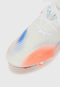 Fußballschuh in Weiß mit einer strukturierten Oberfläche. Hervorgehoben durch einen blauen und orangefarbenen Farbverlauf, weiße Schnürsenkel und sichtbare Stollen an der Sohle.