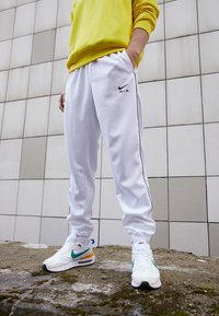 Vita Nike Air-byxor med svarta sidostrimmor och logotyp, kombinerat med vita och flerfärgade Nike-sneakers. Overdelen är en gul tröja.