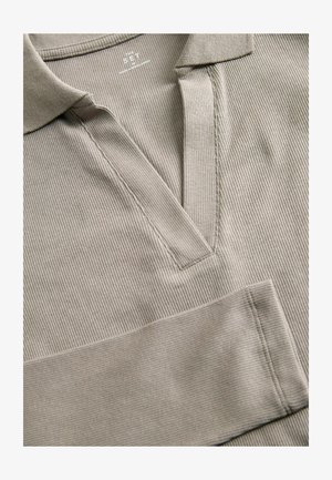 Beige ribbattu pologejp, jolla on V-kaula-aukko, ja jossa on teksturoitu kangas sekä näkyvät ompeluyksityiskohdat napituksessa ja hihoissa.