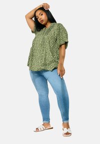 Grönmönstrad blus med korta ärmar, matchad med ljusblå slim fit jeans och vita slidesandaler. Slätt tyg, avslappnad passform.