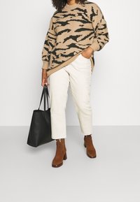 Suéter de punto beige con rayas de tigre negras, pantalones crema con dobladillos deshilachados, botas de tacón marrones y un bolso tote negro.