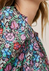 Blusa floral con un fondo oscuro y coloridas flores moradas, azules y rojas, delicada vegetación y una textura de tela suave y ligera.