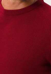 Czerwony sweter dziewiarski z prążkowaną fakturą, okrągłym dekoltem i rękawami raglanowymi. Tkanina wygląda na miękką i wygodnie dopasowaną.