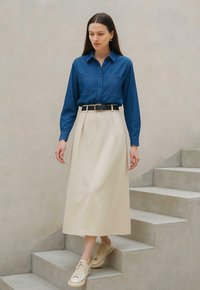 Denim button-up shirt with two chest pockets, paired with a beige knee-length skirt, cinched with a black belt, and beige sneakers.