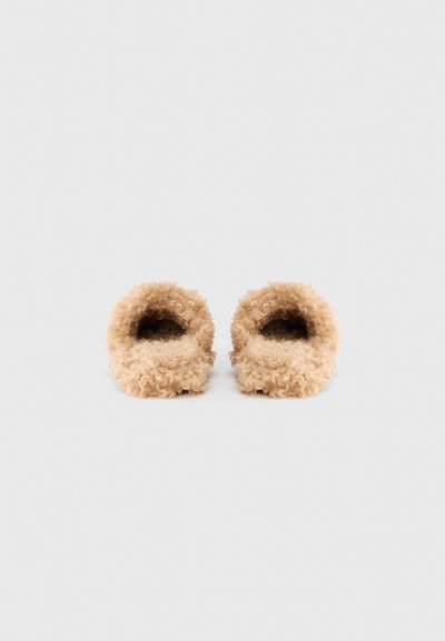 Chaussons en fourrure beige avec une texture douce et duveteuse. Conception à dos ouvert et avant arrondi. Construction légère, adaptée à une utilisation intérieure.