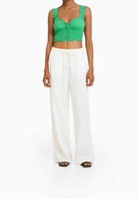 Zielony krótki top z falbankami na ramiączkach i guzikami z przodu, zestawiony z białymi spodniami szerokimi na nogawkach. Całość uzupełniają płaskie czarne sandały.