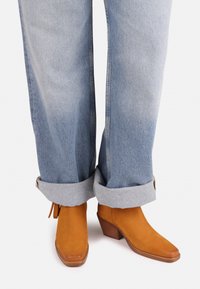 Ruske ankle boots med firkantet tå og blokkhæl, parret med falmede lyseblå vidde jeans med opprullede kanter.