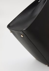 Zwarte leren tote bag met een gestructureerd ontwerp, voorzien van gouden hardware accenten en een gladde textuur. Schone lijnen benadrukken minimalisme.