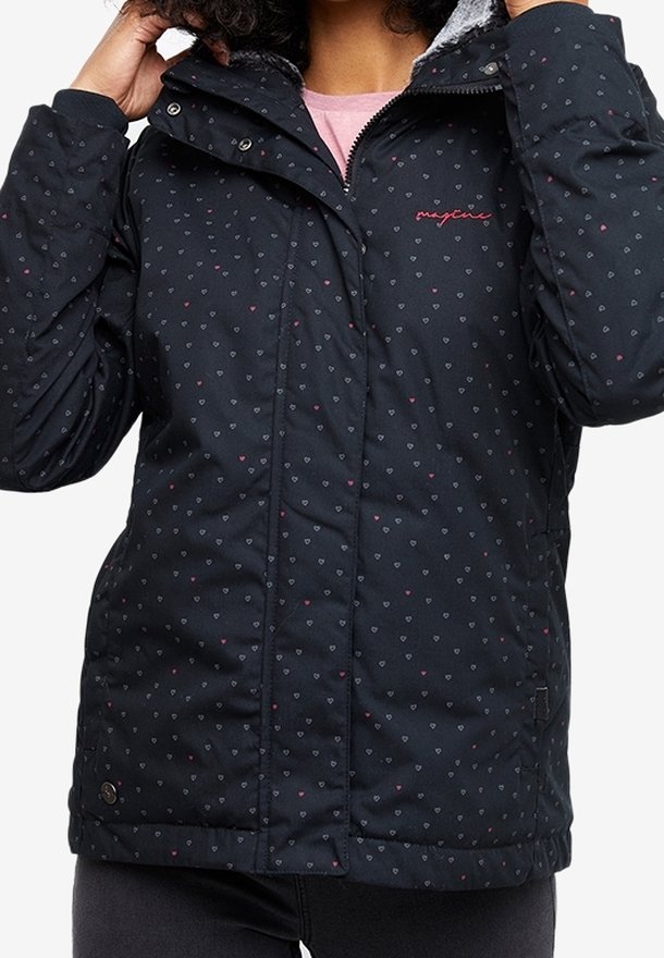 Femme portant une veste matelassée noire avec de petits motifs de cœur et un logo rose sur la poitrine, ajustant le col de la capuche.