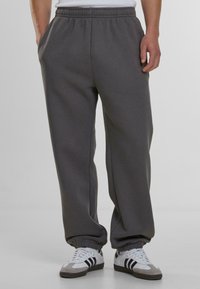 Pantalones de chándal grises con un corte relajado, cintura elástica y tobillos acampanados, hechos de material suave. Combinados con zapatillas deportivas blancas.