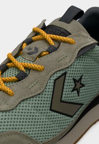 Πράσινο αθλητικό παπούτσι από δίχτυ με επικαλύψεις από ελιά γκρίζας σουέντ, κίτρινα κορδόνια με μαύρες κηλίδες και μαύρο λογότυπο αστέρι στο πλάι.