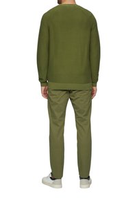 Pull en tricot vert olive avec un col rond, accompagné d'un pantalon assorti vert olive et de baskets blanches avec des accents bleu marine.
