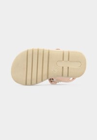 Λαστιχένια σόλα ενός μπεζ παιδικού σανδαλιού μεγέθους 20, με ανάγλυφο μοτίβο αντιολισθητικής επιφάνειας στο κάτω μέρος.