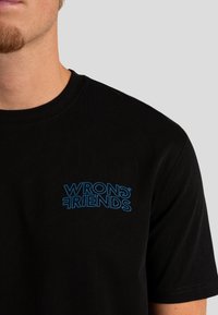 Czarny bawełniany t-shirt z niebieskim nadrukiem graficznym "WRONG FRIENDS" na lewej klatce piersiowej. Krótkie rękawy, okrągły dekolt.