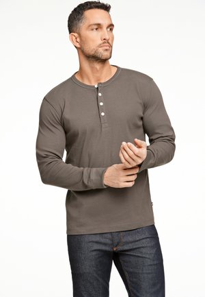 Donkergrijze langslavige henley-shirt van zachte stof, met een drieknoopsluiting en fitted mouwen, gecombineerd met donkere spijkerbroek.
