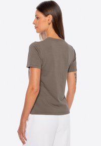 Khaki t-shirt z krótkim rękawem, okrągłym dekoltem, minimalną teksturą i czystymi liniami. Materiał wydaje się być miękki i dopasowany w okolicy ramion.