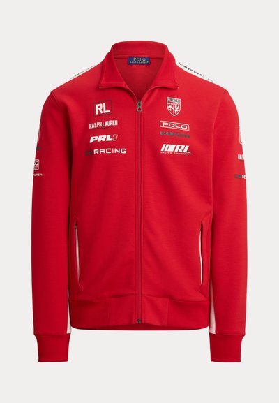 Červená bunda na zips s vysokým golierom. Vyrobená z mäkkej látky, má biele akcenty, viacero log a bočné vrecká so zipsom.