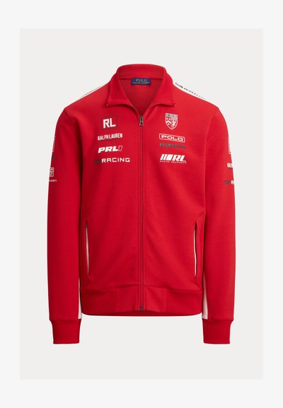 Rdeča zadrga jakna z visokim ovratnikom. Narejena iz mehkega blaga, vsebuje bele detajle, več logotipov in stranske žepke z zadrgo.