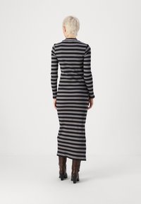 Vestido de manga longa listrado em preto e cinza com um silhueta ajustada, textura canelada e uma bainha até ao chão. Combinado com botas de salto castanhas.