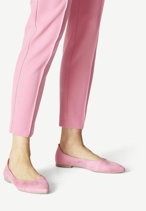 Różowe zamszowe baleriny z zaokrąglonym noskiem i niskim obcasem, zestawione z różowymi, dopasowanymi spodniami. Gładka faktura i minimalistyczny design.