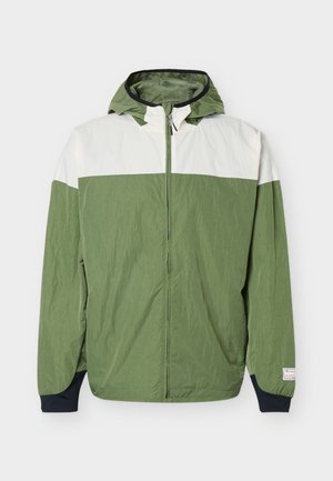 Kerge lukuga kapuutsiga jakk rohelise kehaosa, valge ülaosa rinnal, mustade varrukakäppade ja võrkkattega kapuutsiga.