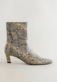 Botín de tobillo de piel de serpiente en tonos marrón y gris, con punta afilada y tacón de bloque de altura media. Superficie texturizada con un patrón de reptil.