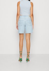 Ljusblå denimshorts med en avslappnad passform, prydda med bakfickor och subtil slitning. Kombinerad med gröna sandaletter med remmar.