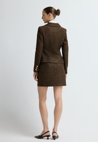 Brązowa marynarka w kratę i pasująca mini spódnica, z złotymi guzikami. Gładka tekstura i dopasowany krój podkreślają zorganizowany design.