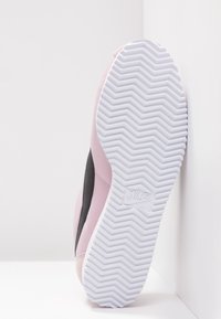 Nike-sneaker med en rosa textilöverkäng och en svart sidopanel. Den vita gummisulan har ett texturerat zickzackmönster.