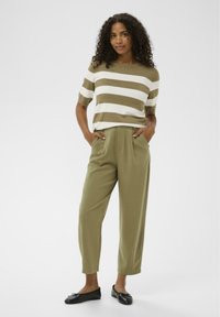 Pull rayé en olive et blanc, associé à un pantalon taille haute olive. Le pantalon comporte des poches latérales ; des chaussures plates noires complètent la tenue.