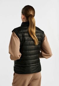 Czarna ocieplana kamizelka z wysokim kołnierzem, z poziomym pikowanym wzorem i błyszczącą teksturą. Podkreślona dopasowanym krojem i bocznymi zamkami błyskawicznymi.