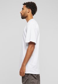 T-shirt en coton blanc à manches courtes et col rond classique, présenté de côté. La coupe est décontractée et le tissu semble doux.