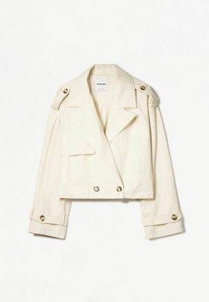 Veste courte en crème faite d'un tissu léger, dotée d'un design croisé, d'épaulières et d'accents de boutons dorés.
