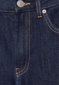 Gros plan sur un jean en denim bleu foncé montrant un bouton métallique, les détails des coutures, une passants de ceinture et une partie de la poche avant avec un rivet.