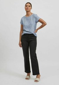 Camisa azul clara con puntos blancos, cuello redondo, mangas cortas, combinada con pantalones vaqueros de talle alto y pata de elefante negros y sandalias beige.