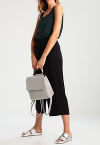 Haut sans manches vert, pantalon noir à jambes larges, sandales plates argentées et sac à dos gris clair au design structuré avec bretelles réglables.