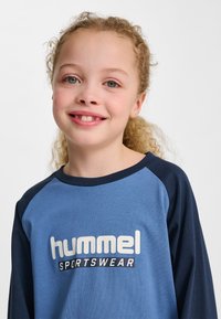 Blå och marinblå långärmad t-shirt med rund halsringning, med en stor "hummel SPORTSWEAR"-logotyp i vitt på framsidan.