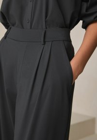 Vysoký pás, tmavosivé nohavice s hladkou textúrou, skladaným dizajnom, bočnými vreckami a strihaným strihom, so pätkou na opasok.