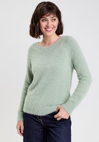 Minzgrüner flauschiger Pullover mit langen Ärmeln und rundem Ausschnitt, der eine weiche Textur und einen lässigen Schnitt aufweist. Getragen mit dunklen Jeans.