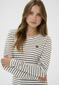 Dlhý rukáv pruhovaná košeľa v bielej a hnedej farbe. Obsahuje malú zelenú srdiečkovú nášivku na hrudníku. Mäkká textúra a dizajn s okrúhlym výstrihom.