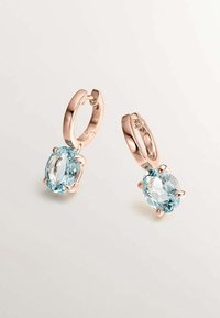 Pendientes de aro en oro rosa con gemas ovaladas de color azul claro, que presentan una superficie facetada y configuraciones de cuatro garras, exhiben un diseño elegante.