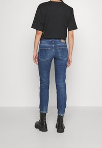 Svart kortärmad t-shirt i kombination med blå slim-fit jeans. Jeans har två bakfickor och en beige märkeslapp vid midjan. Svarta ankelboots.