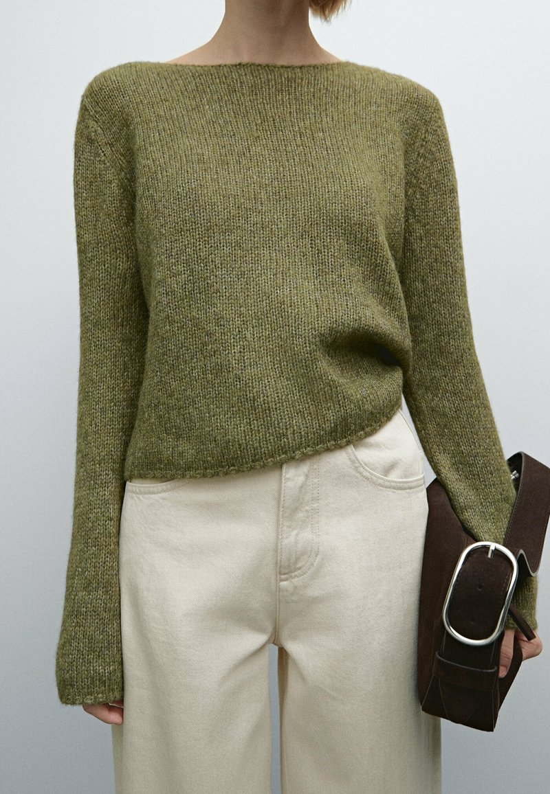 Olive green knitted sweater with a boat neckline, loose fit, and ribbed texture, paired with cream-colored wide-leg pants and a dark brown bag.
