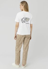 T-shirt en coton blanc présentant un design imprimé noir d'une figure et d'un cœur au dos. Associé à un pantalon de pyjama à imprimé léopard beige.