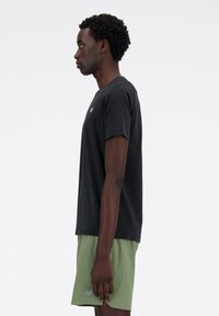 Black short-sleeve T-shirt with a round neckline, worn with light green athletic shorts; features a subtle logo on the chest.
