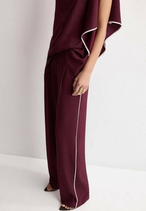 Pantalones de pierna ancha en color burdeos con ribete lateral blanco, de textura suave y diseño plisado. Combinados con una blusa fluida y zapatos de tacón abiertos.